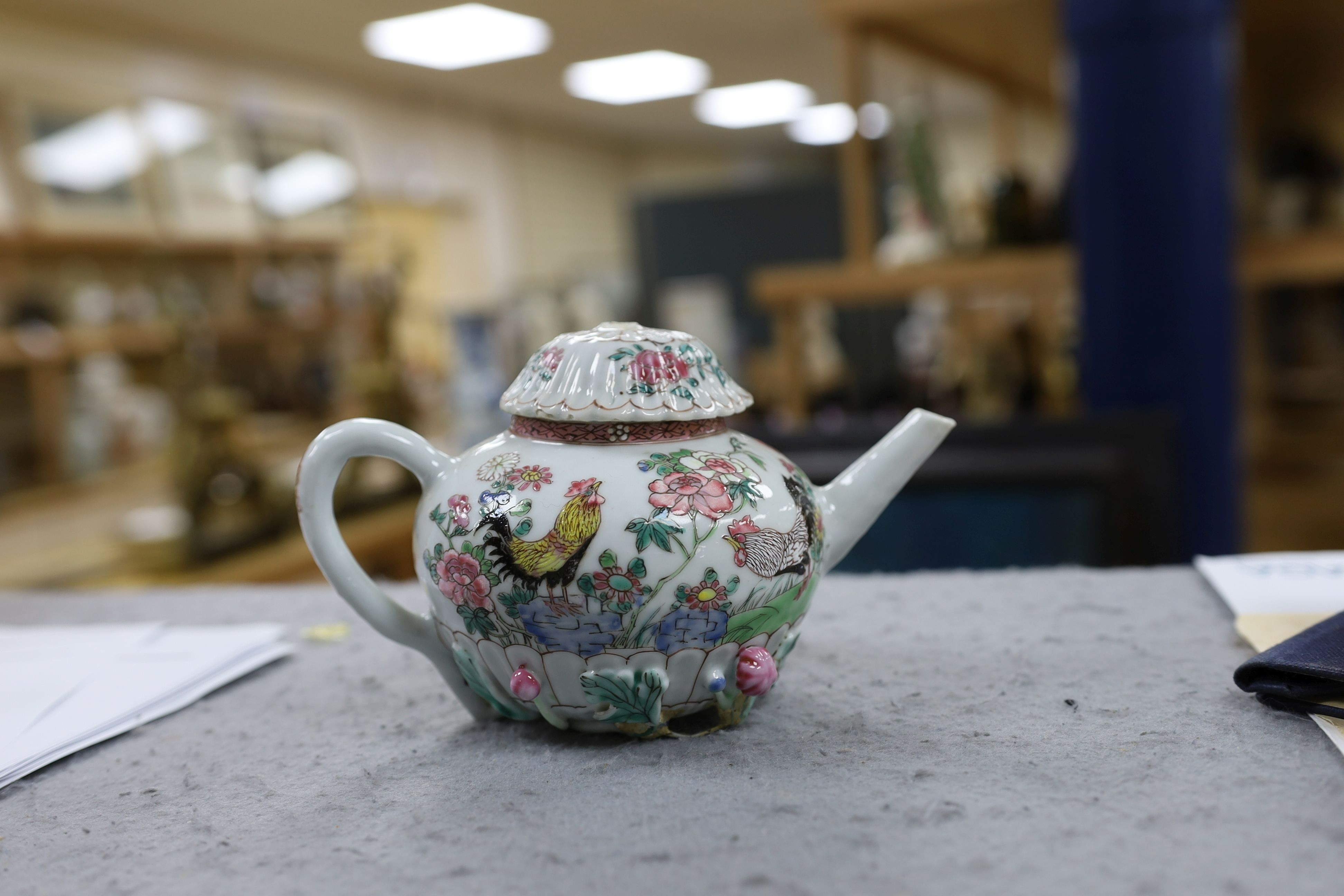 A Chinese famille rose chrysanthemum moulded teapot, early Qianlong period, painted with a cockerel amongst flowers, on a cage work base, 10 cms high